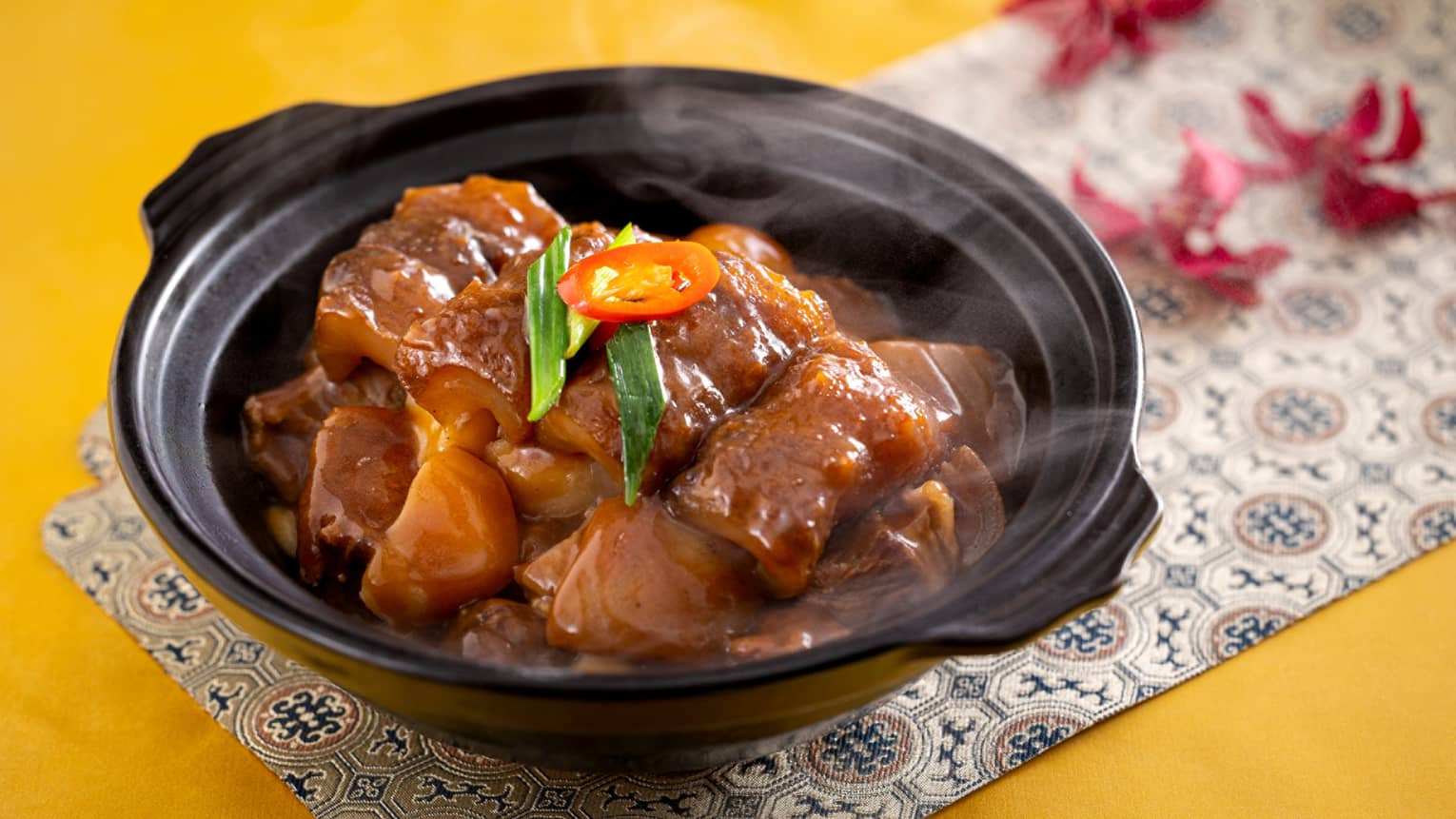 ,A steaming hot meat dish garnished with green onion and chili pepper