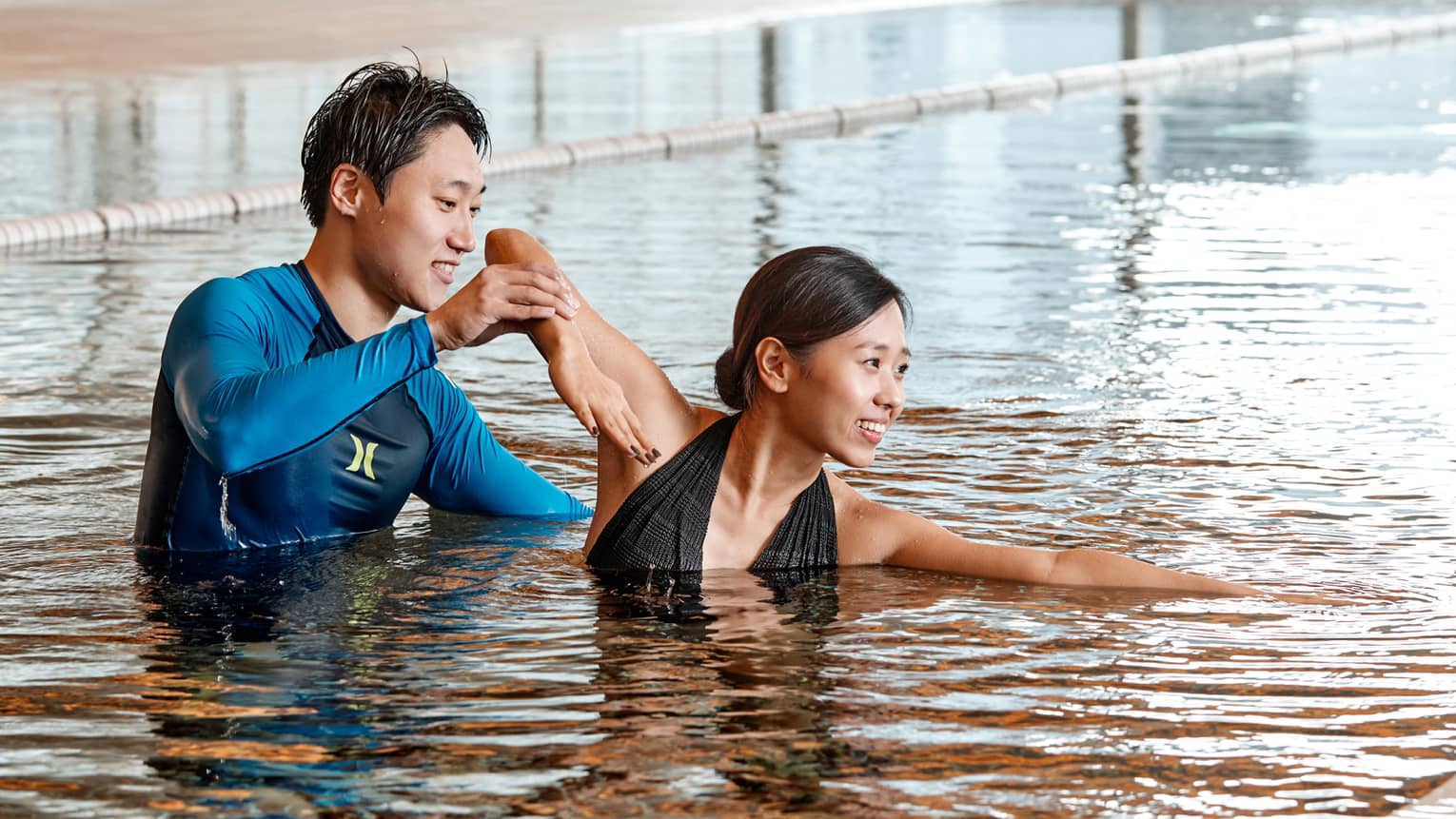 Swimming instructor helps woman position arm in indoor swimming pool