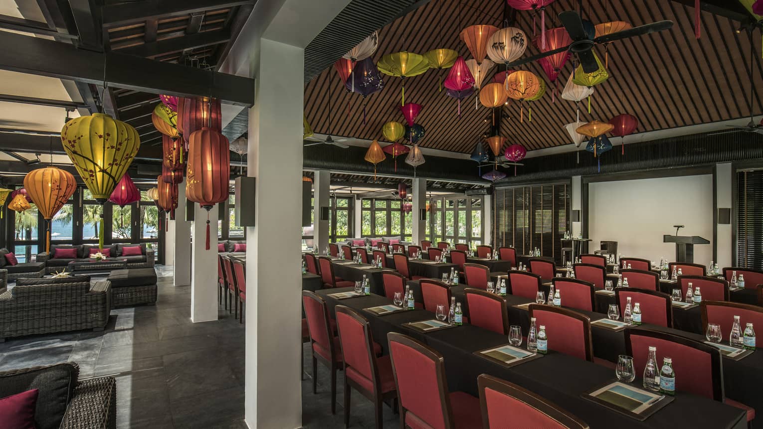 Meeting room by ocean with long tables, chairs, couches, wooden ceiling, colourful paper lanterns