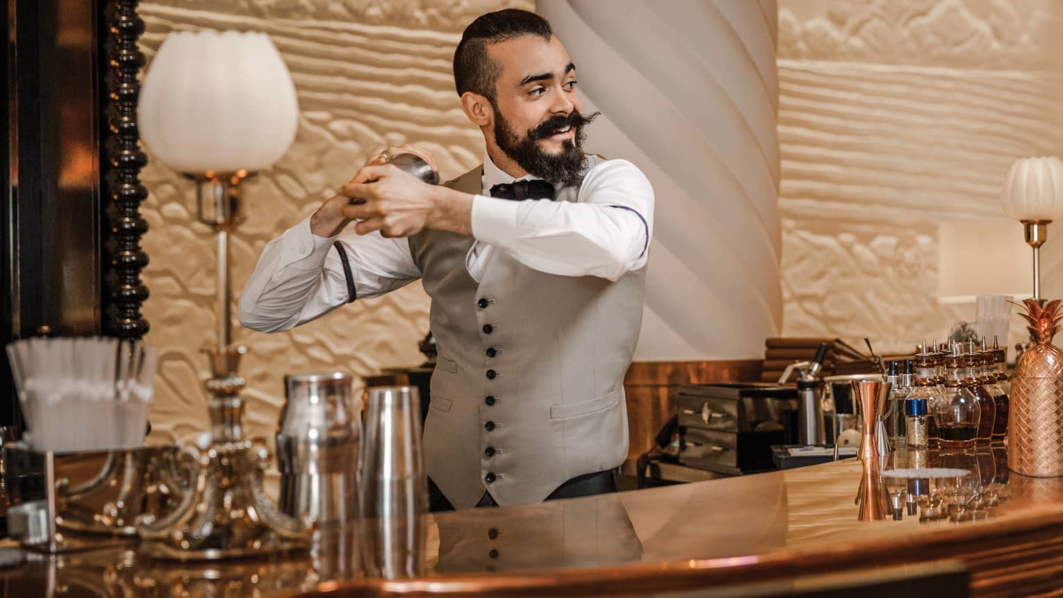 Mixologist with beard and waxed mustache, vest shakes cocktail behind bar