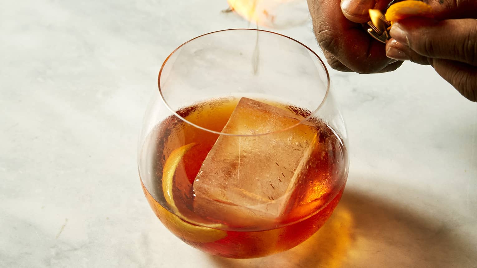 Hands hovering over a bronze cocktail in a clear glas sitting on marble counter