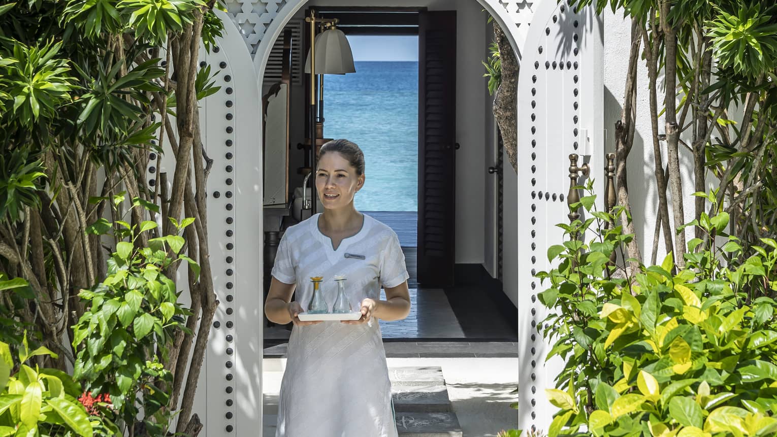 A four seasons spa member carries a tray of food through a shrubbery lined archway 