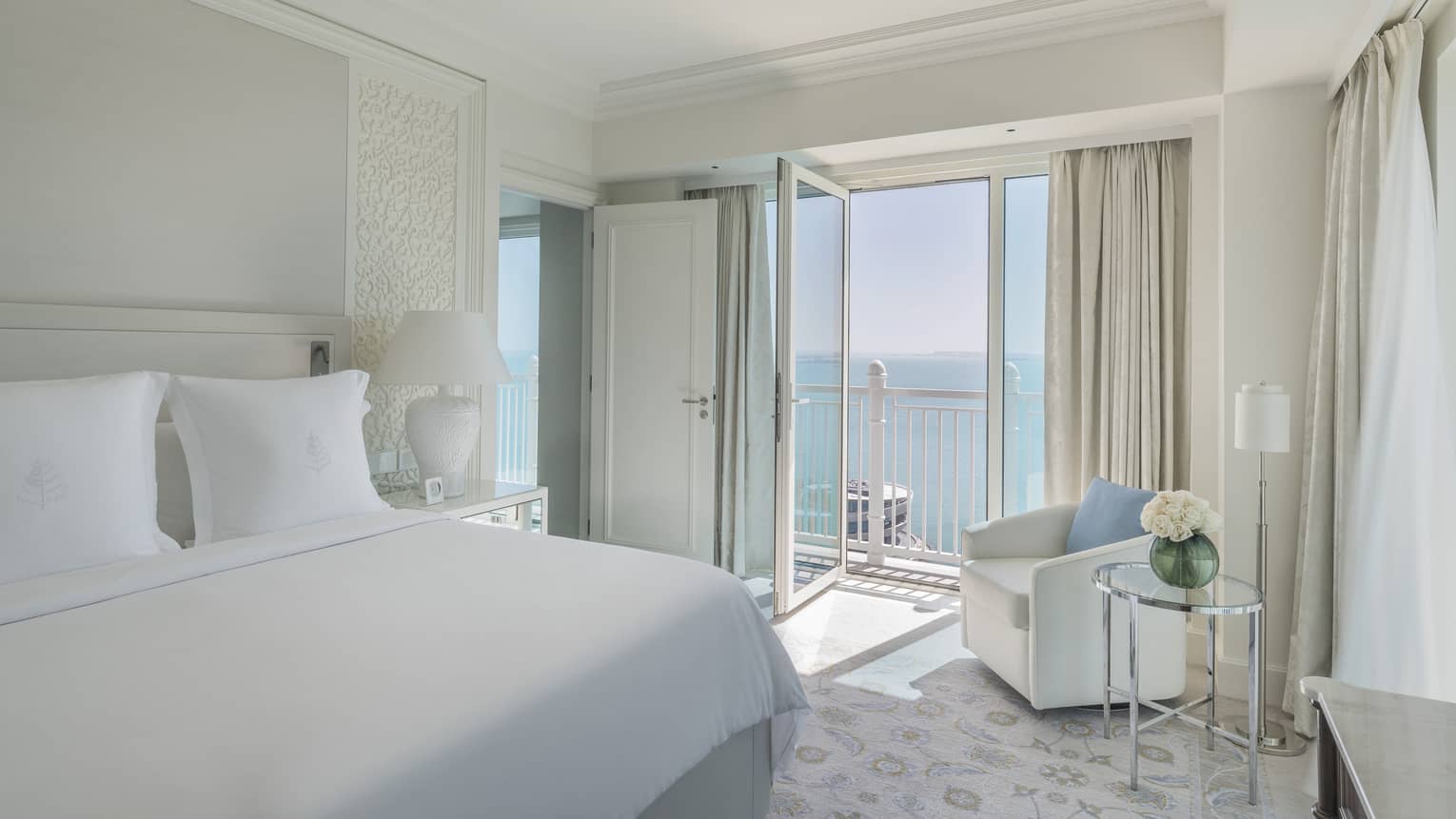 A suite with a large white bed, and an open balcony overlooking the sea.