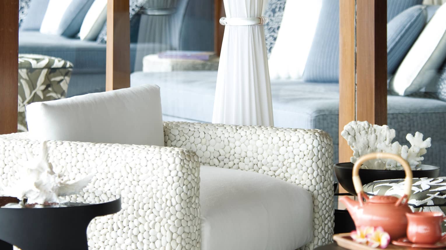 Close-up of white stone armchair with white cushion, tea pots on table