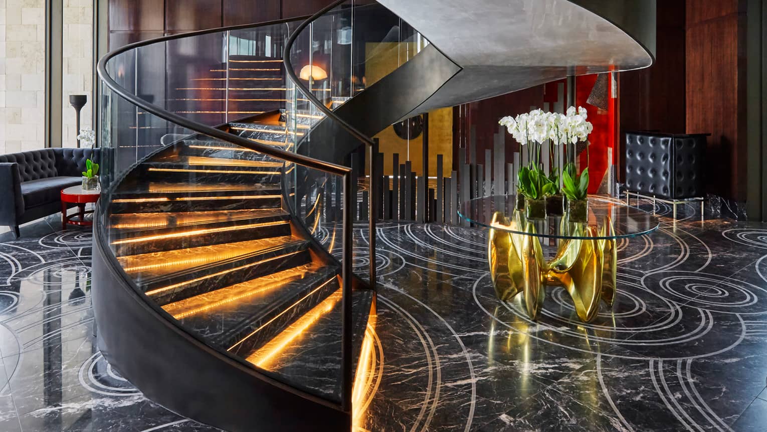 Spiral staircase with black marble steps with orange lights, glass railings, black marble lobby with flowers