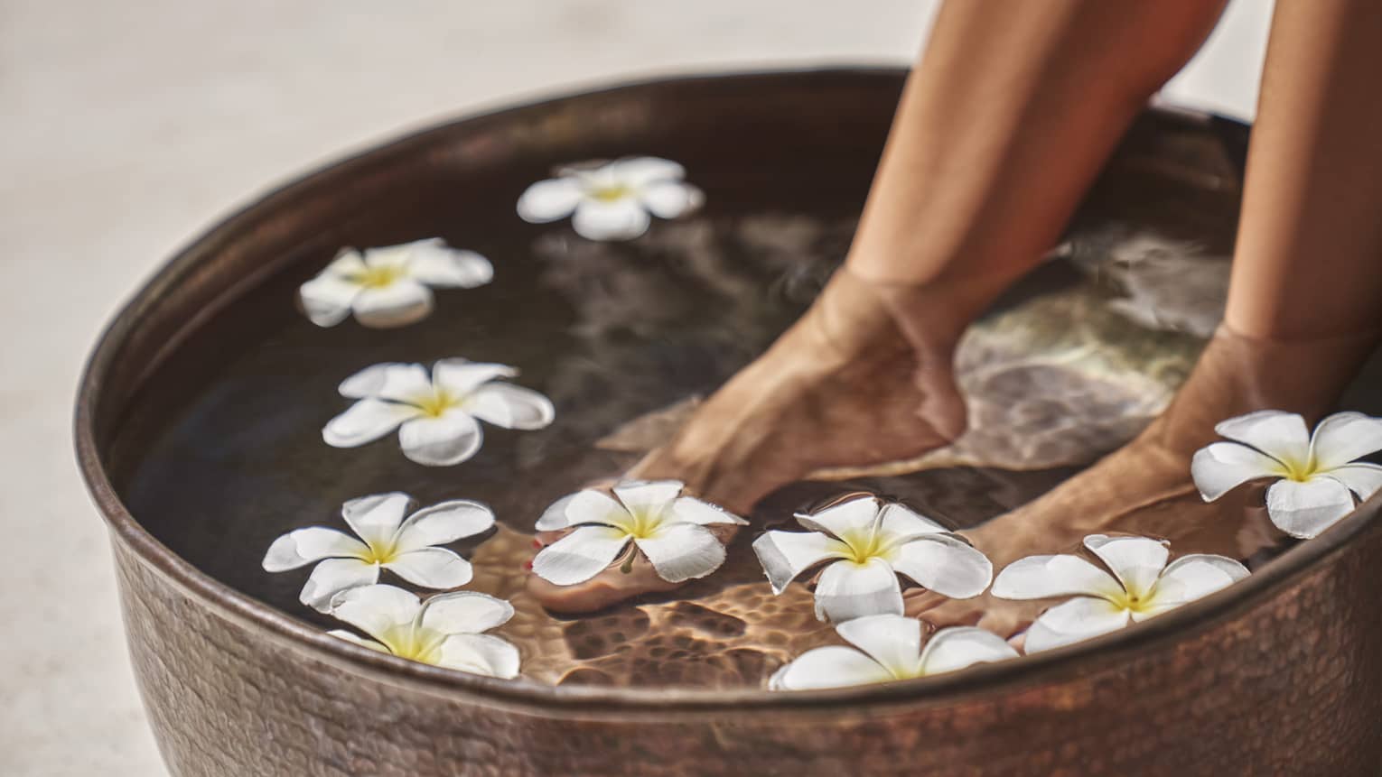 A woman's feet in a bowl of water and flowers.