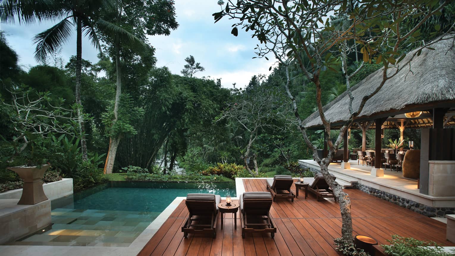 Outdoor patio and pool of the Royal Villa, surrounded by trees, dining room under thatched roof