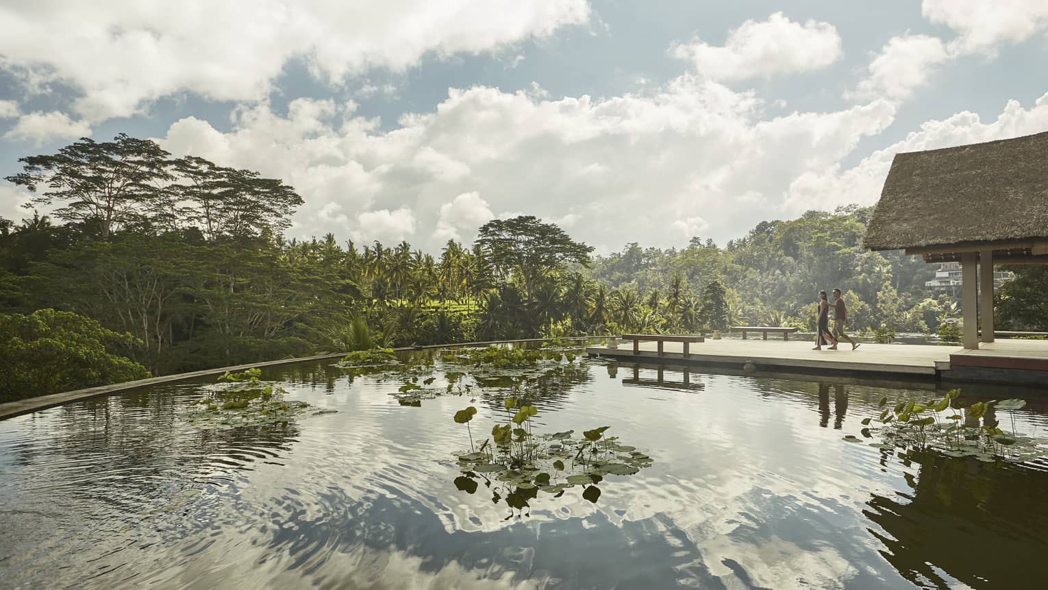 Reflection of clouds in lotus pond on rooftop as man and woman walk by on wood footpath