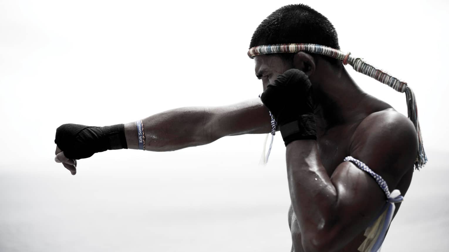 Muay Thai boxer punching, silhouetted by a white-grey background