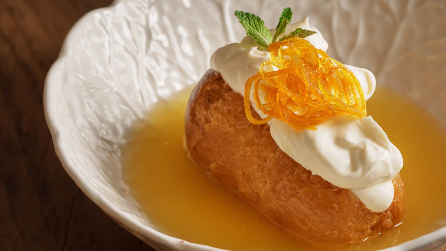 Orange-flavoured dessert in small white bowl topped with whipped cream and mint sprig