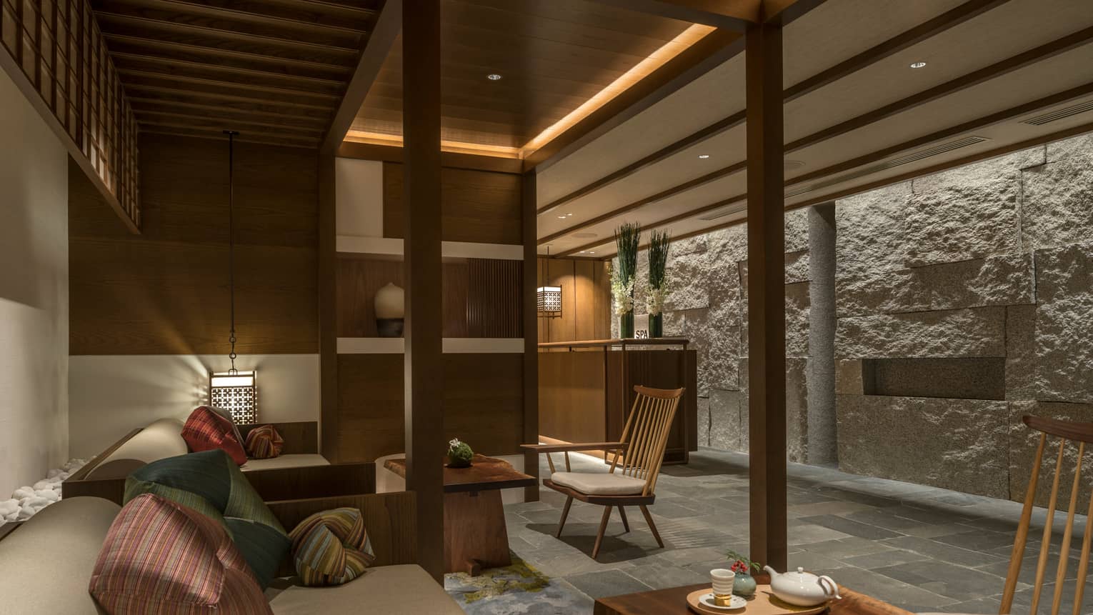 Spa lounge with plush bench, cushions, tea on table, lanterns, rock wall