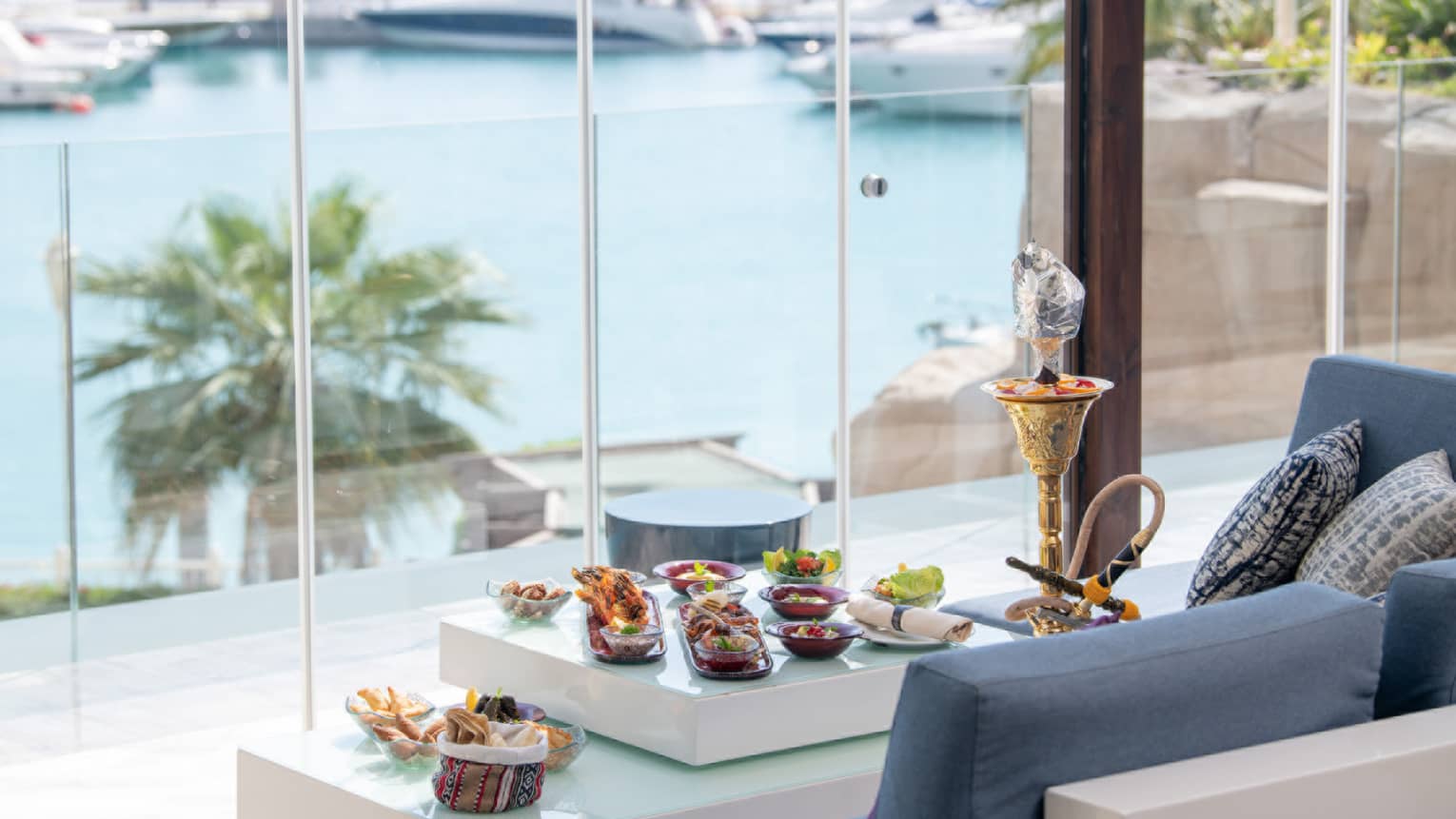 View of the marina through floor-to-ceiling windows at The Terrace, shisha and canap�s on table in front of blue sofa lounge