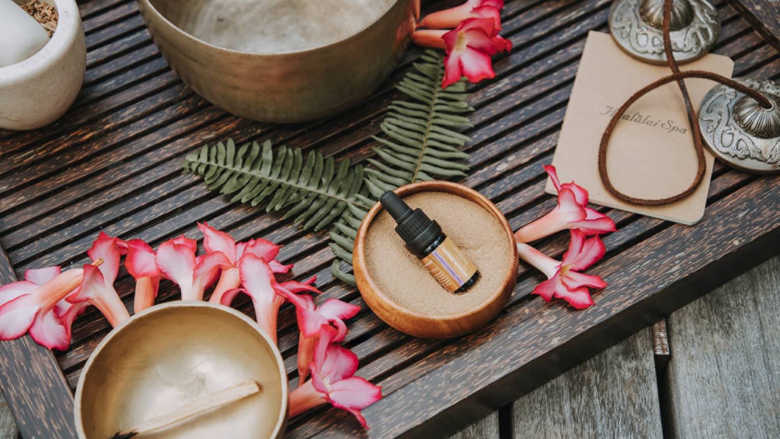 A vial of sandalwood oil, on a wooden table surrounded by vibrant flowers 