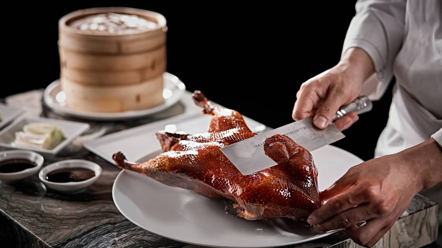 Chef slices Yu Yuan Beijing Duck with large butcher's knife near bamboo basket