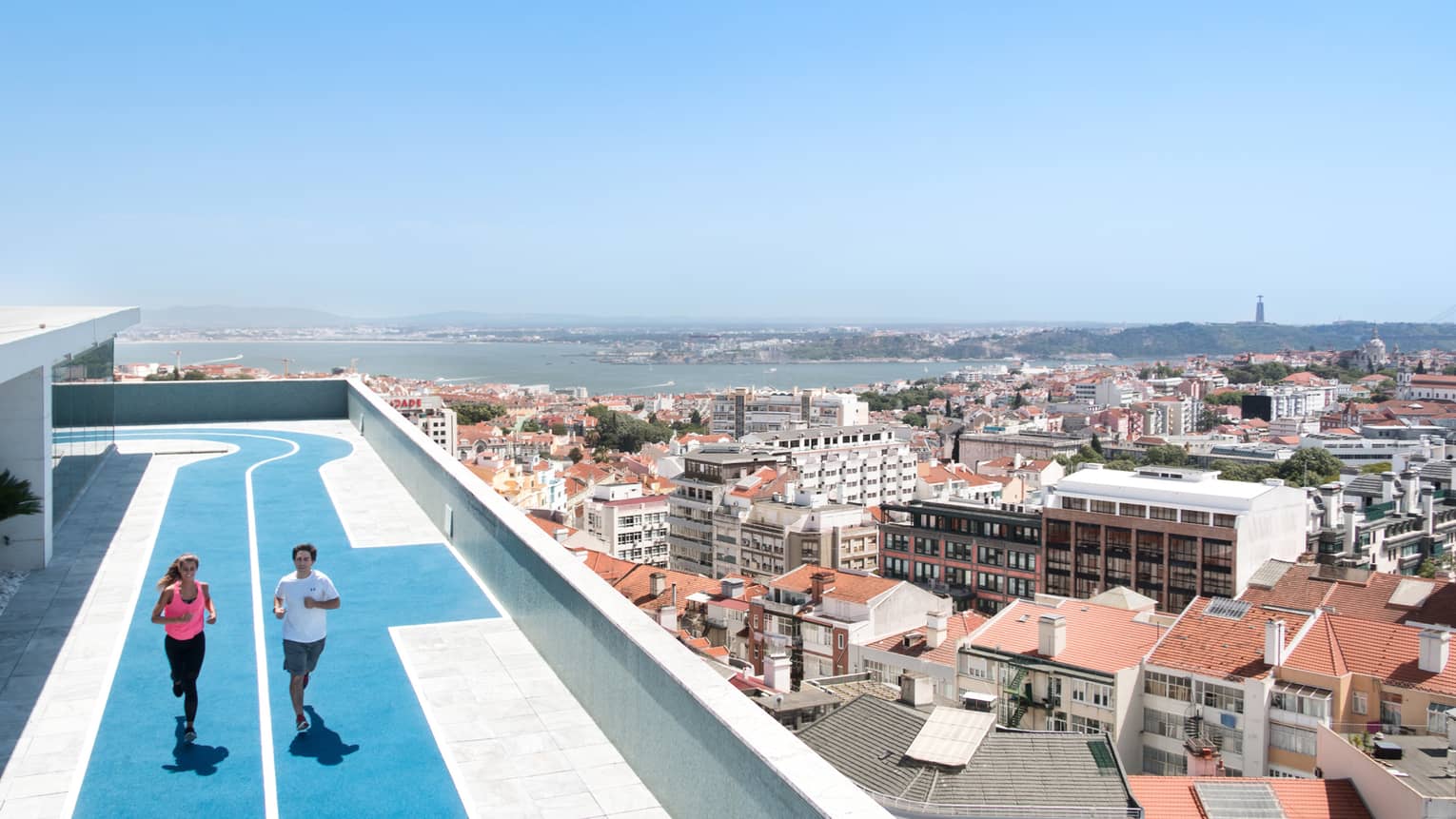 Two people run on blue, rooftop running track, overlooking Lisbon