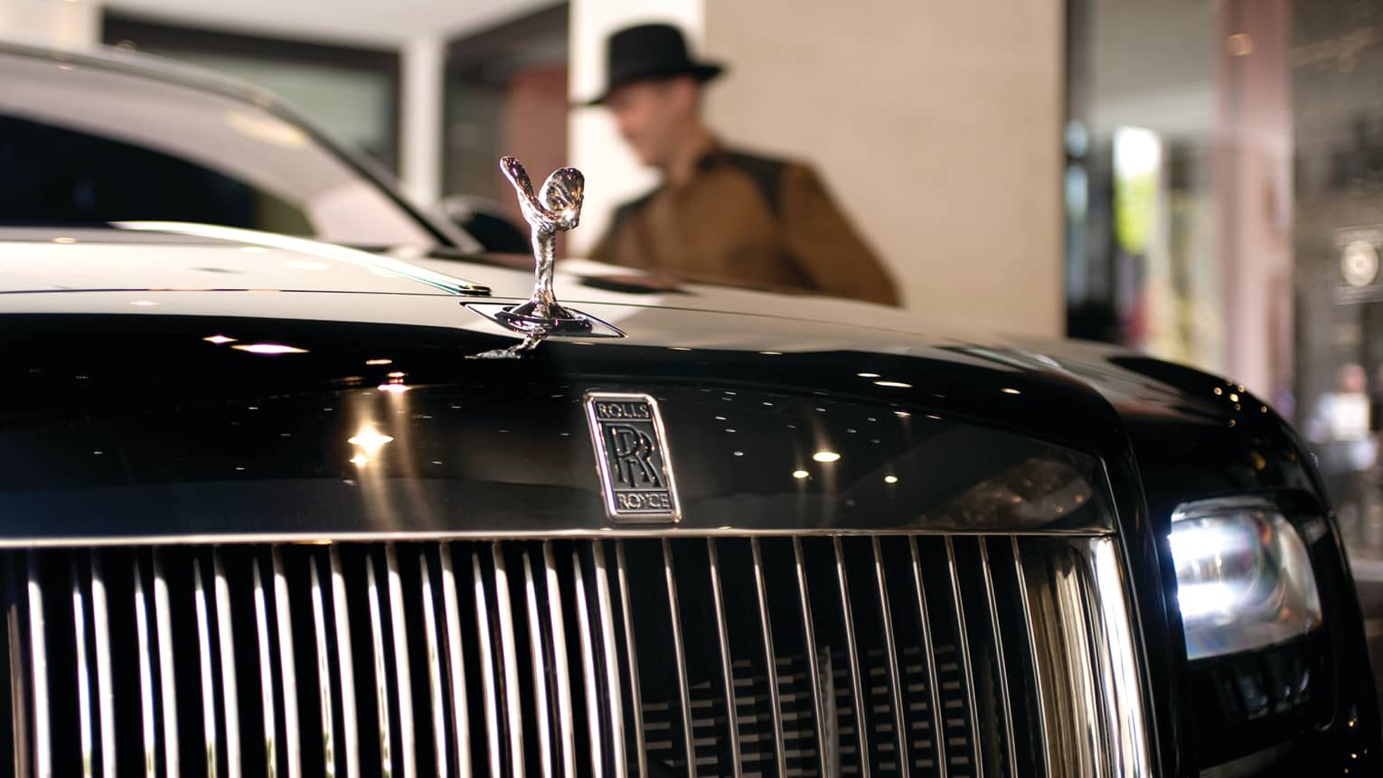 Close-up of Rolls Royce luxury car front grill, man in top hat in background