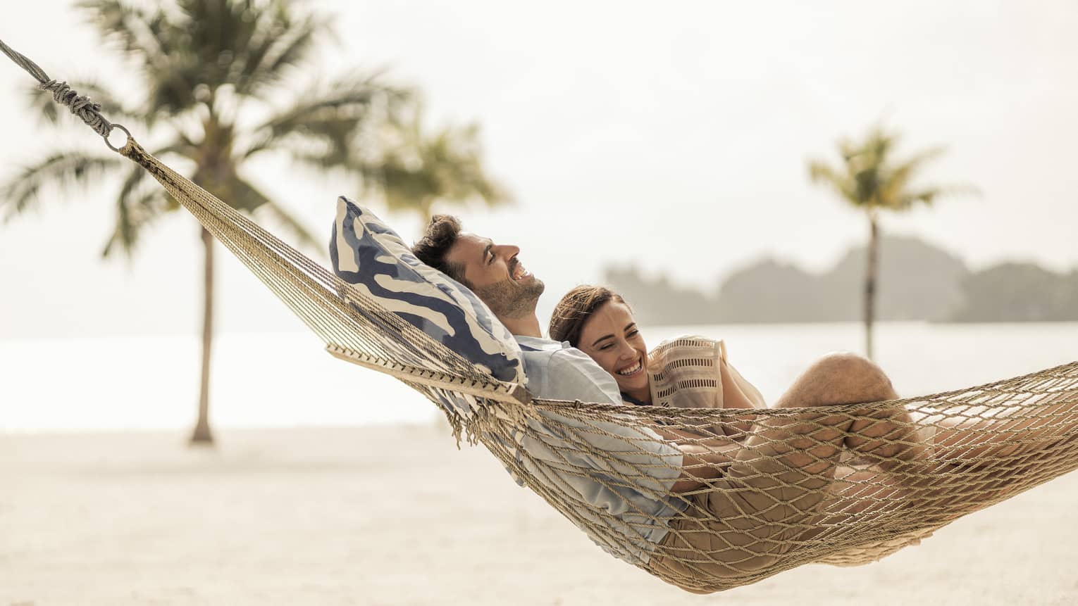 Couple lounges in hammock on sand beach