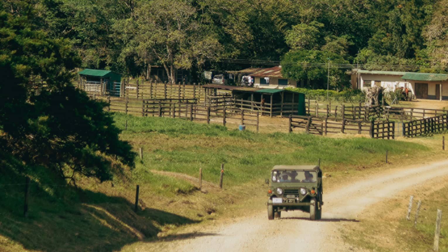 A vintage-style jeep rides along a dirt road, passing by a small farm in the hilly Costa Rican countryside