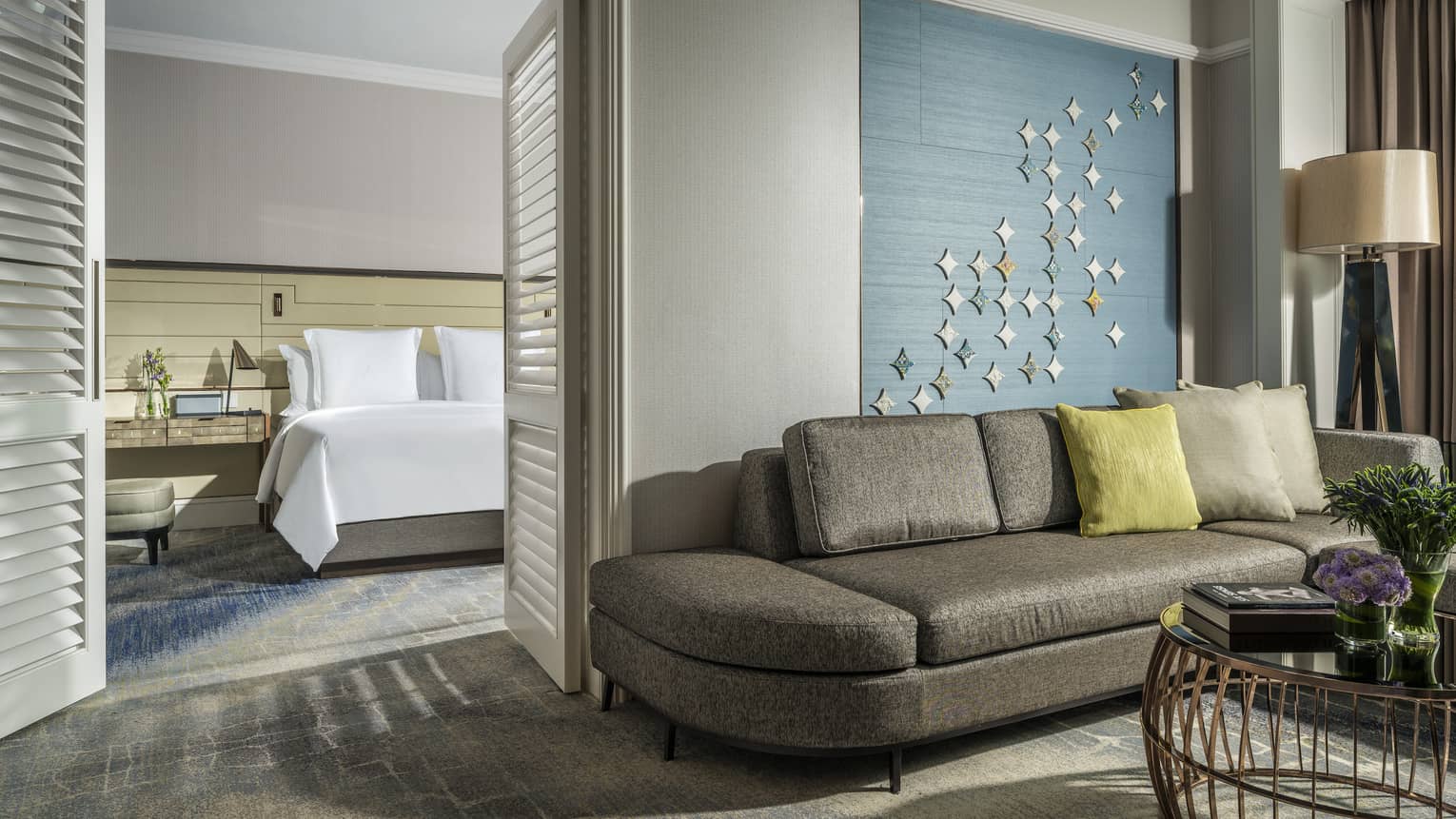 One Bedroom Suite bed in room behind wood shutters, modern grey sofa under textiles