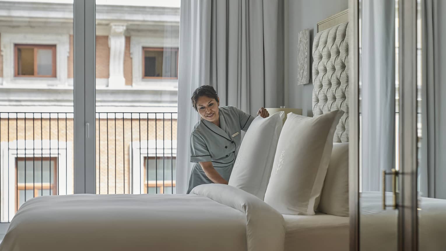 Female housekeeping worker tidies pillow in a hotel room