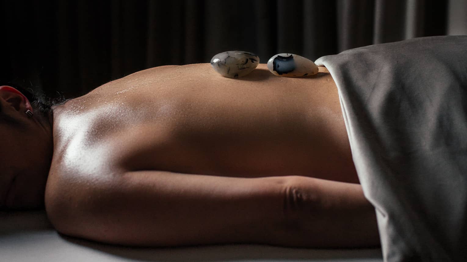 A woman with small stones on her back in a spa treatment room.