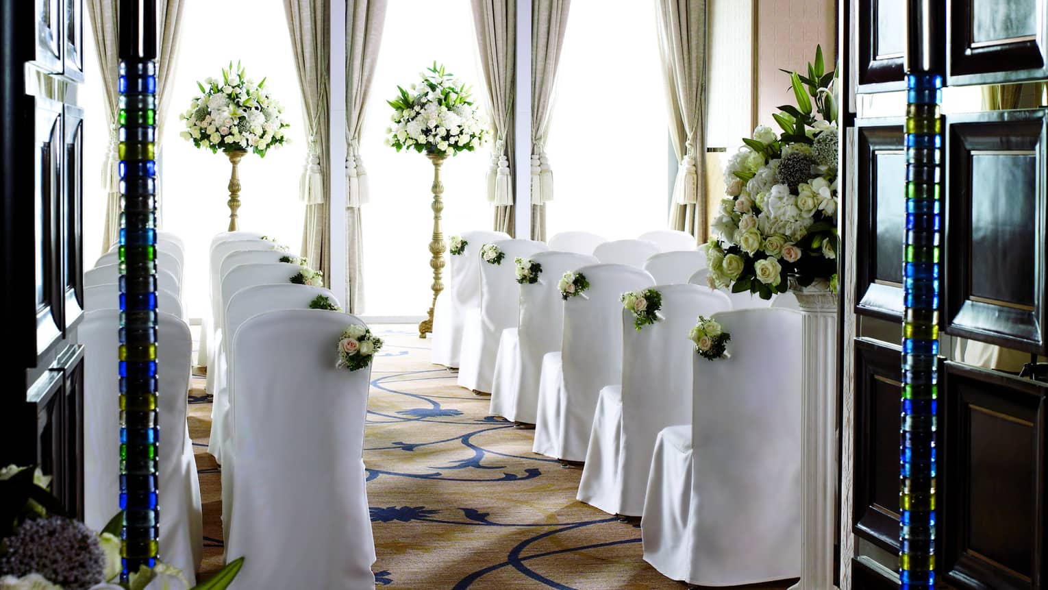 Ballroom wedding ceremony, rows of chairs with white linens face sunny window