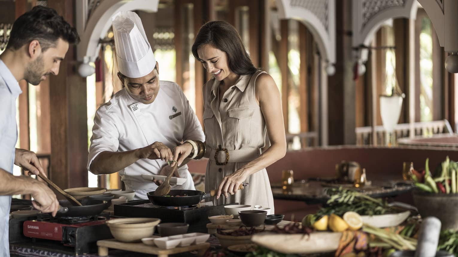 A chef doing an interactive cooking lesson with a man and a woman at the Four Seasons Langkawi
