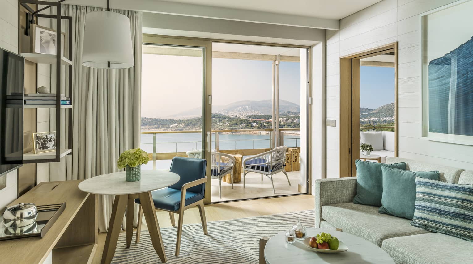 Suite with cream sofa, blue accent pillows and wall art, oval coffee table, round table for one, sliding glass doors leading to balcony, ocean views