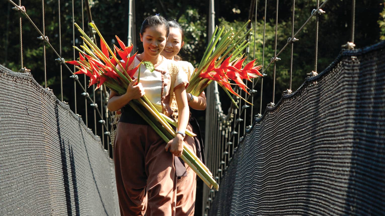 Two women walk down bridge holding bouquets of long-stemmed tropical flowers