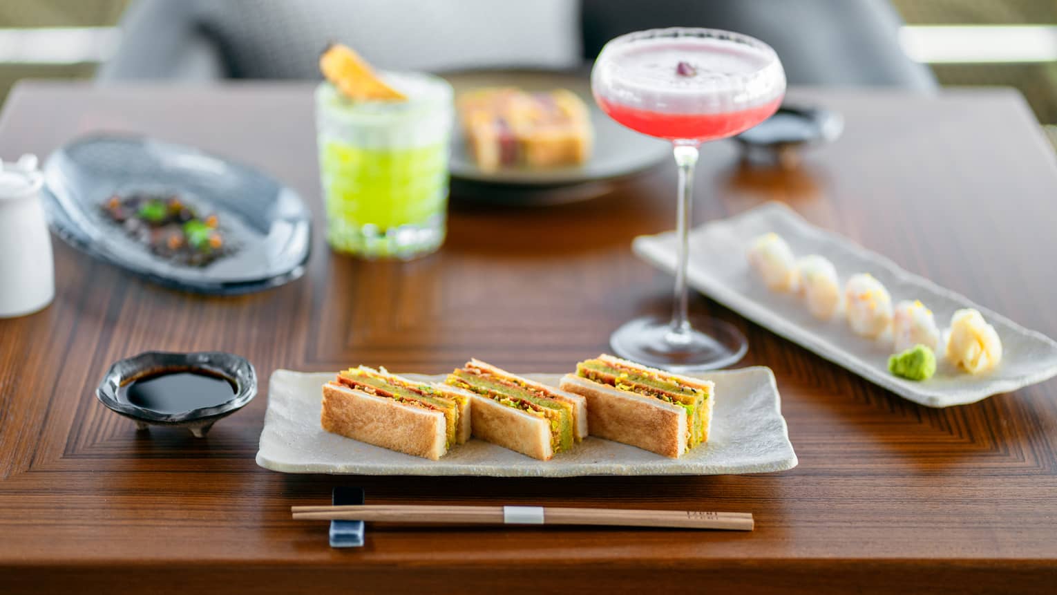 Various small bites on two rectangular dishes with tall red cocktail in between