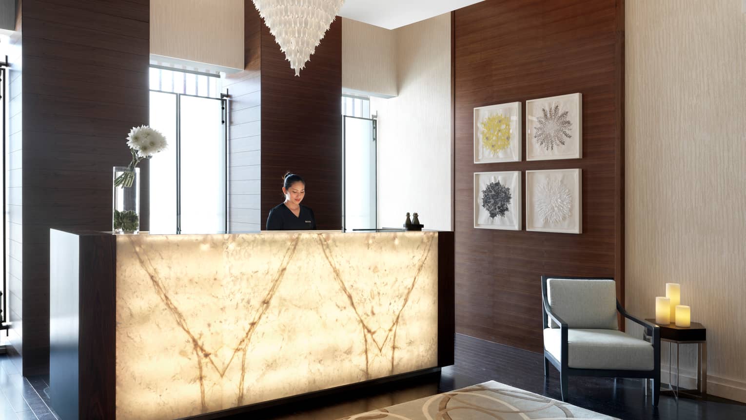Woman stands at illuminated spa lobby reception desk in front of sunny windows