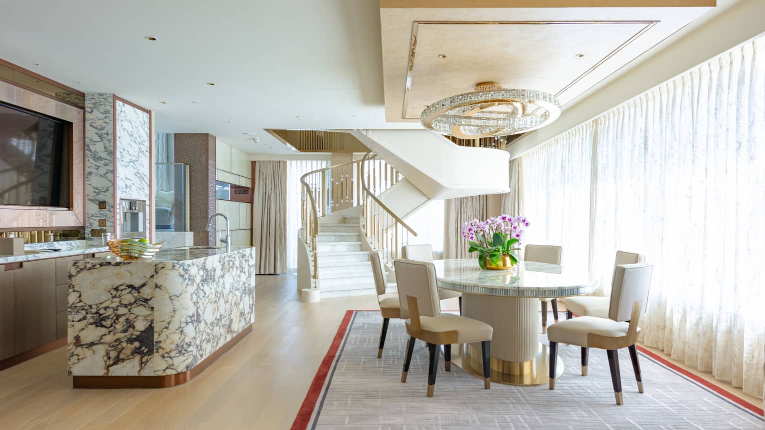 Dining area with round table and four chairs, chandelier, marble counter, spiral staircase in background