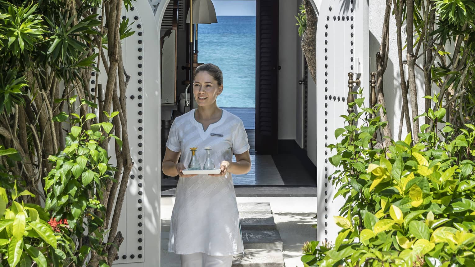 A four seasons spa member carries a tray of food through a shrubbery lined archway 