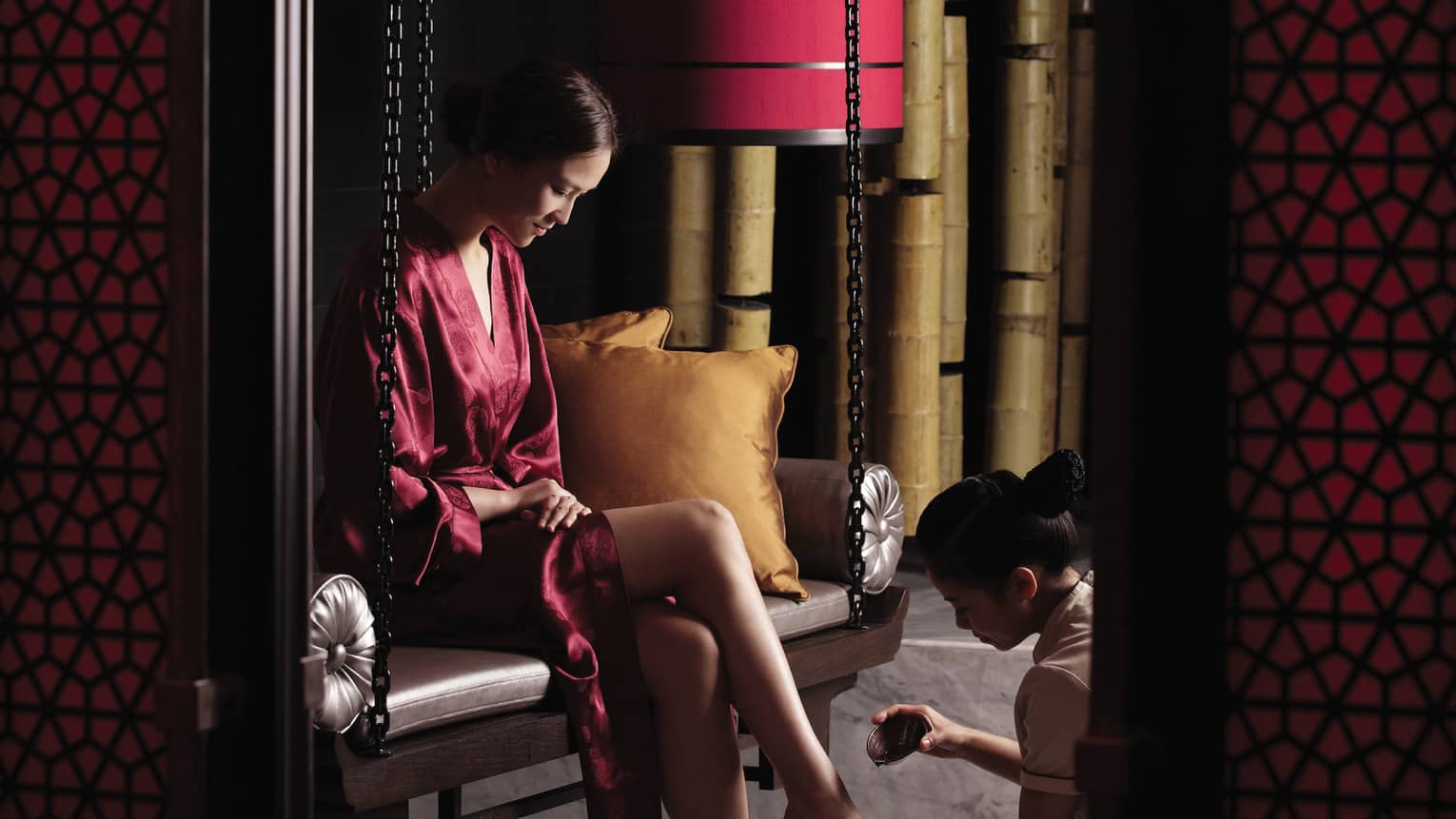 Woman in red silk robe sits on bench as Tranquil Spa staff pours oil on foot