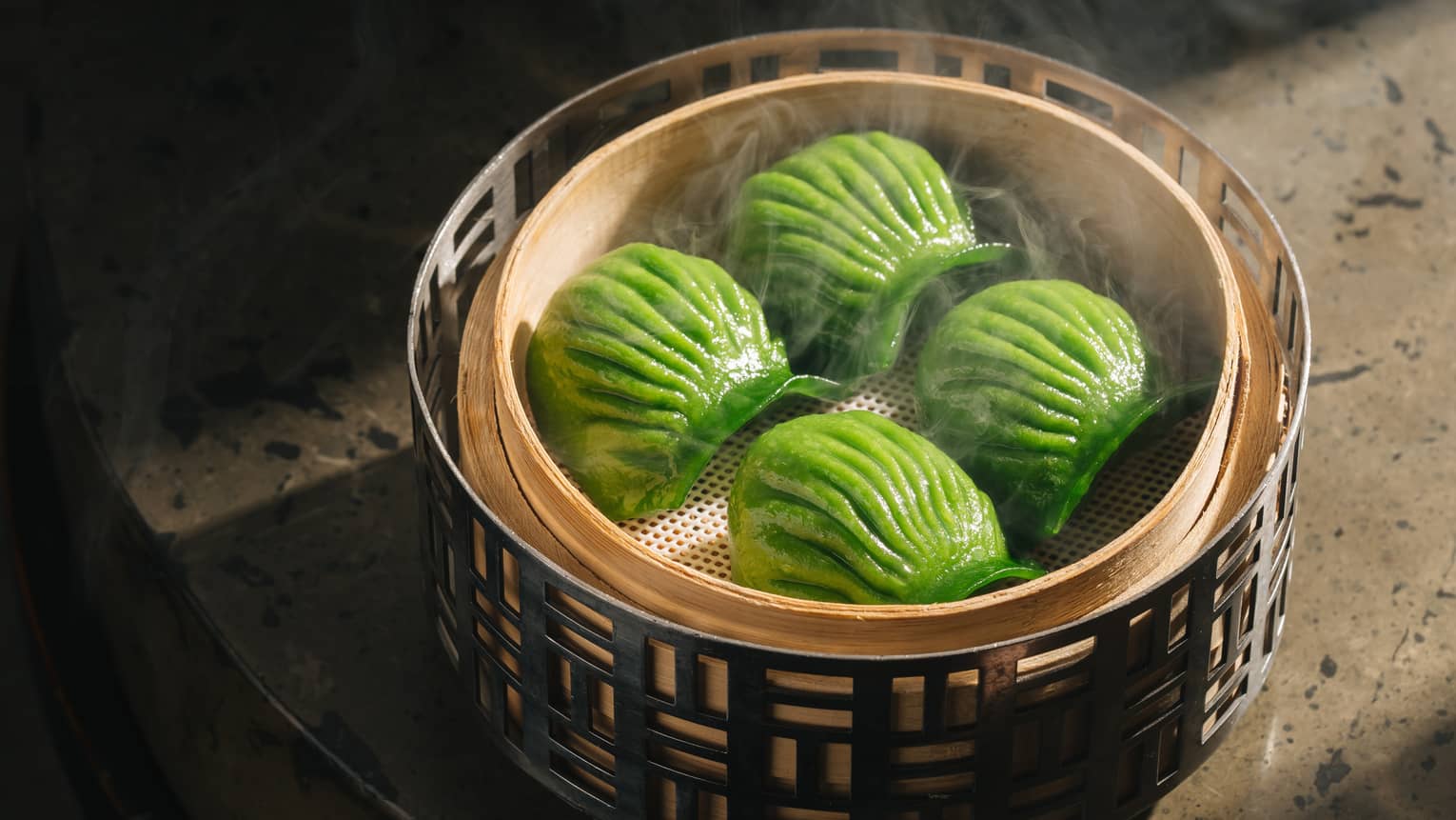 Four green shell-shaped dumplings in traditional bamboo steamer