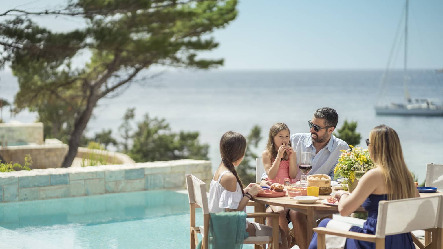 Family of five enjoys a meal outside next to the plunge pool, a sailboat on the Mediterranean in the background