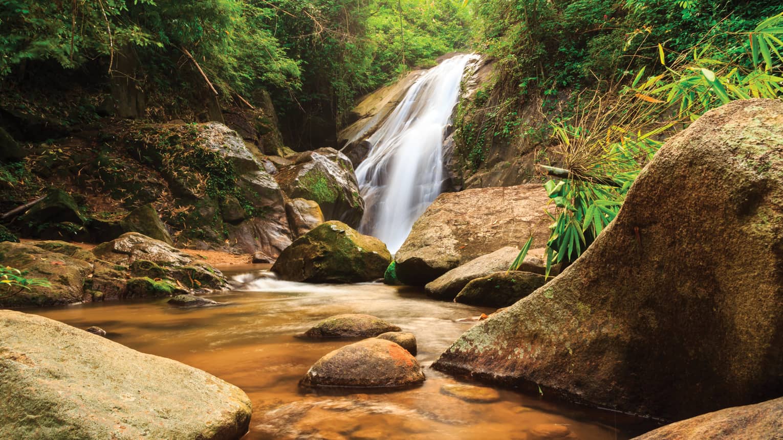 Serene waterfall in the Thai jungle, green foliage, rocks