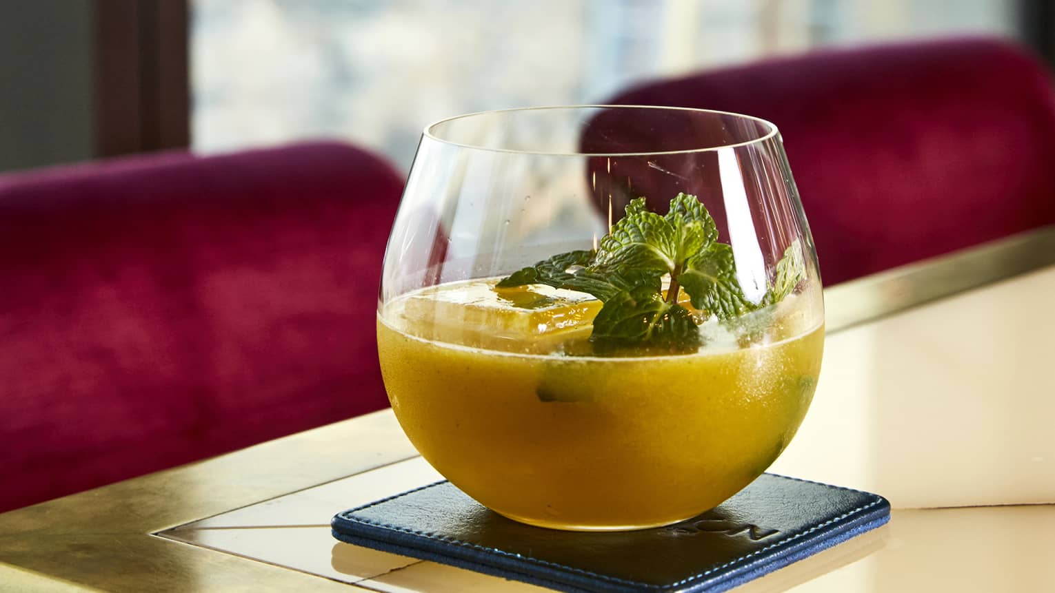 An orange beverage in a rounded glass topped with several sprigs of mint.