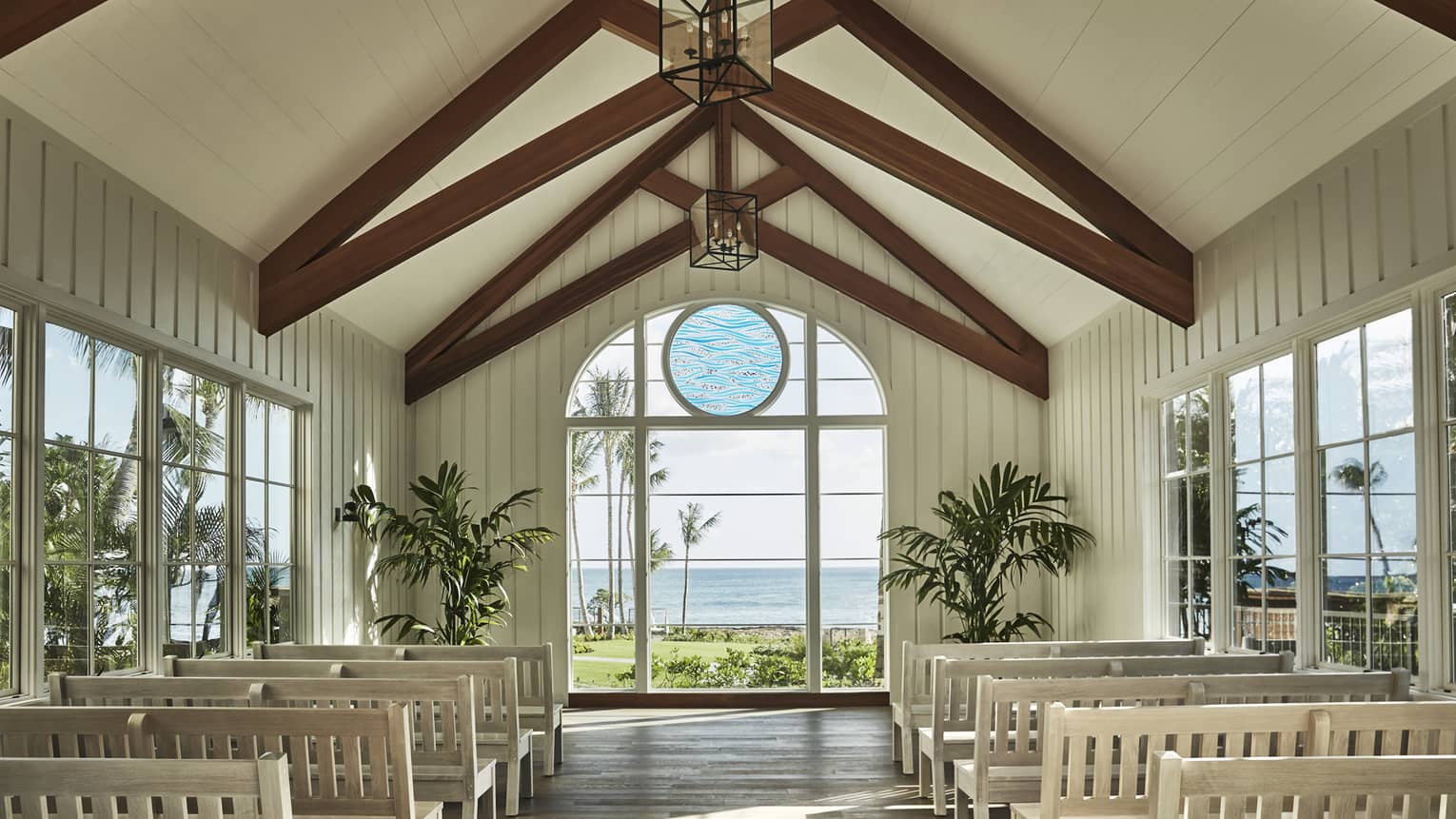 White pews line bright wedding chapel, ocean view through arched window