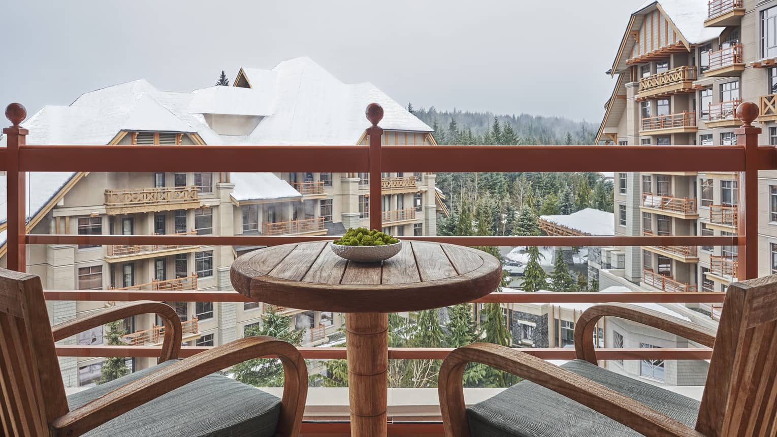 Two wooden arm chairs and a small table on a balcony overlooking Four Seasons Resort Whistler