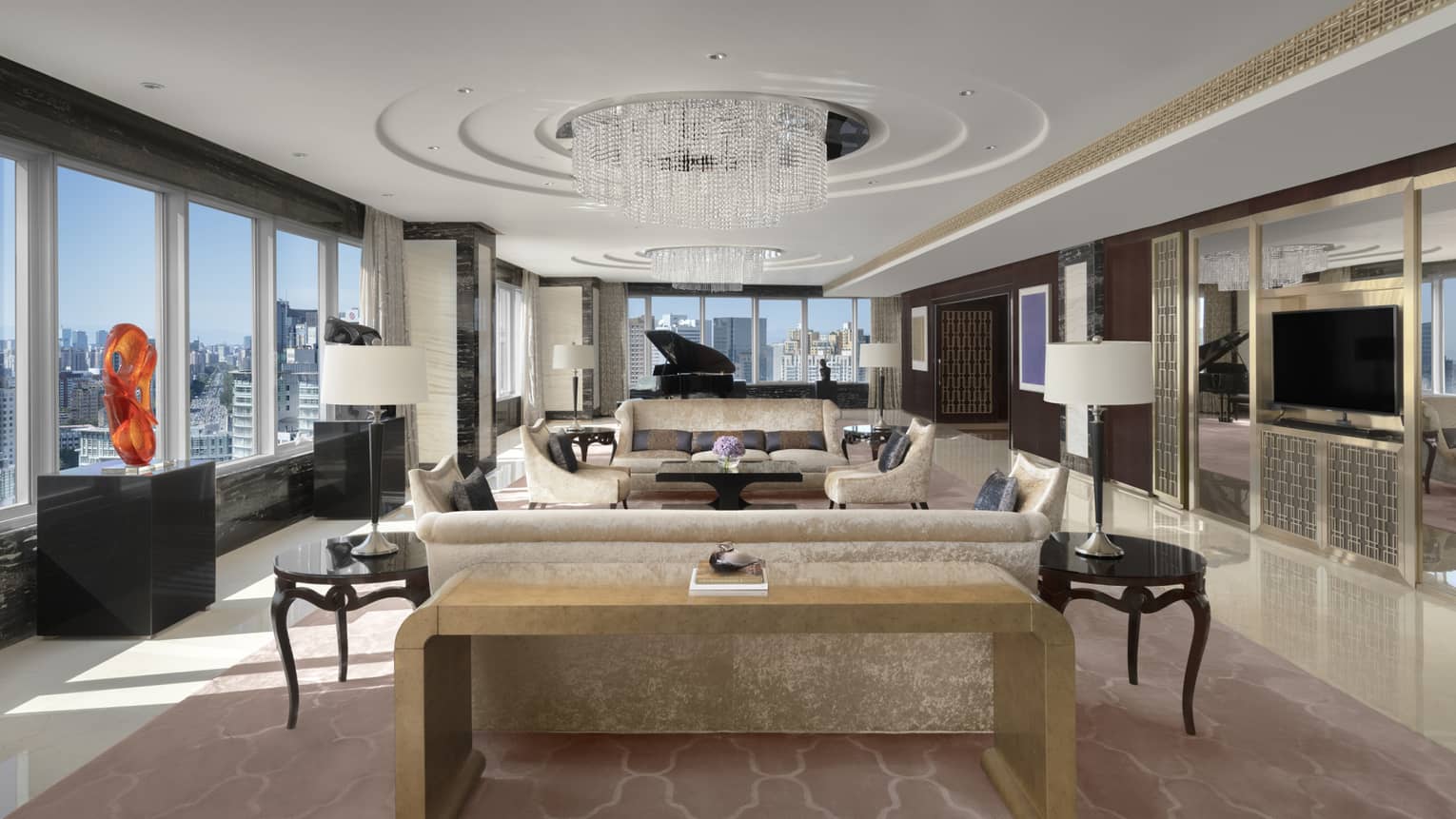 Lavish living room with circular chandelier, two sofas, red sculpture on display, walls of windows