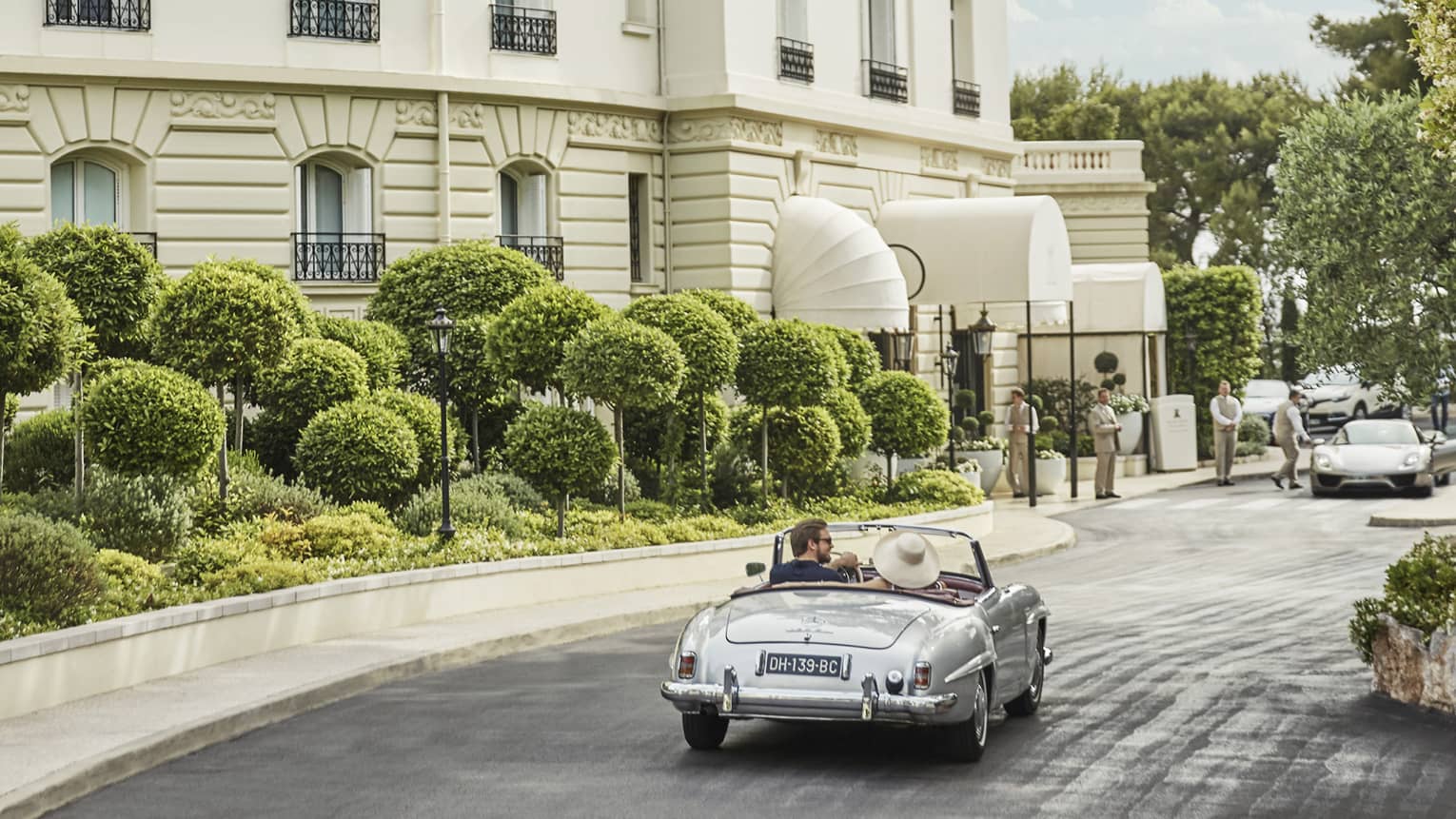 Back view of couple driving luxury convertible bar along sunny city road 