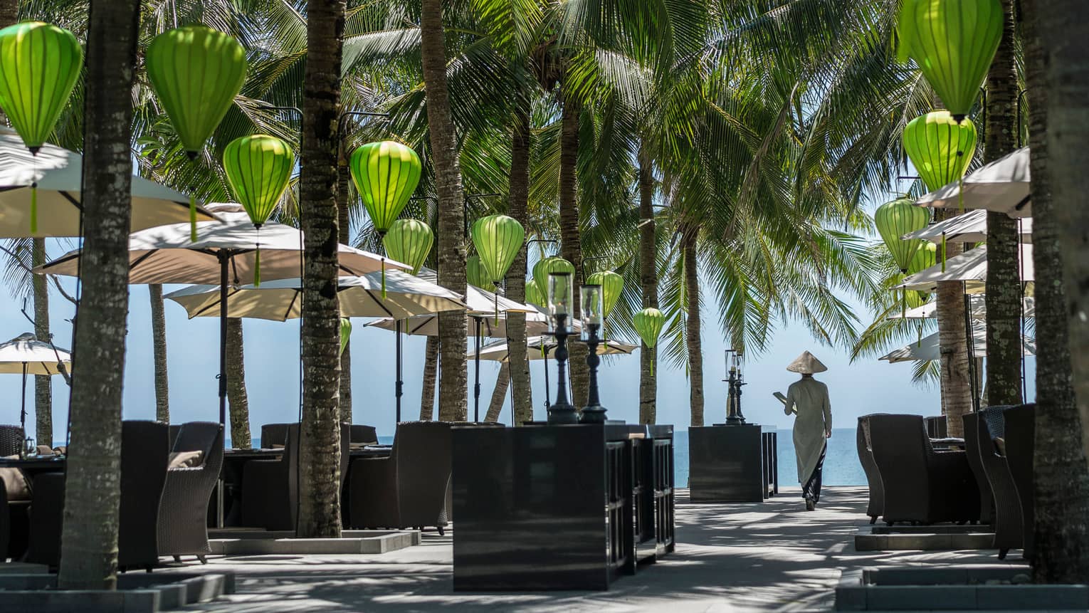 La Sen restaurant patio during day, woman holding menu passes tables, palms, paper lanterns