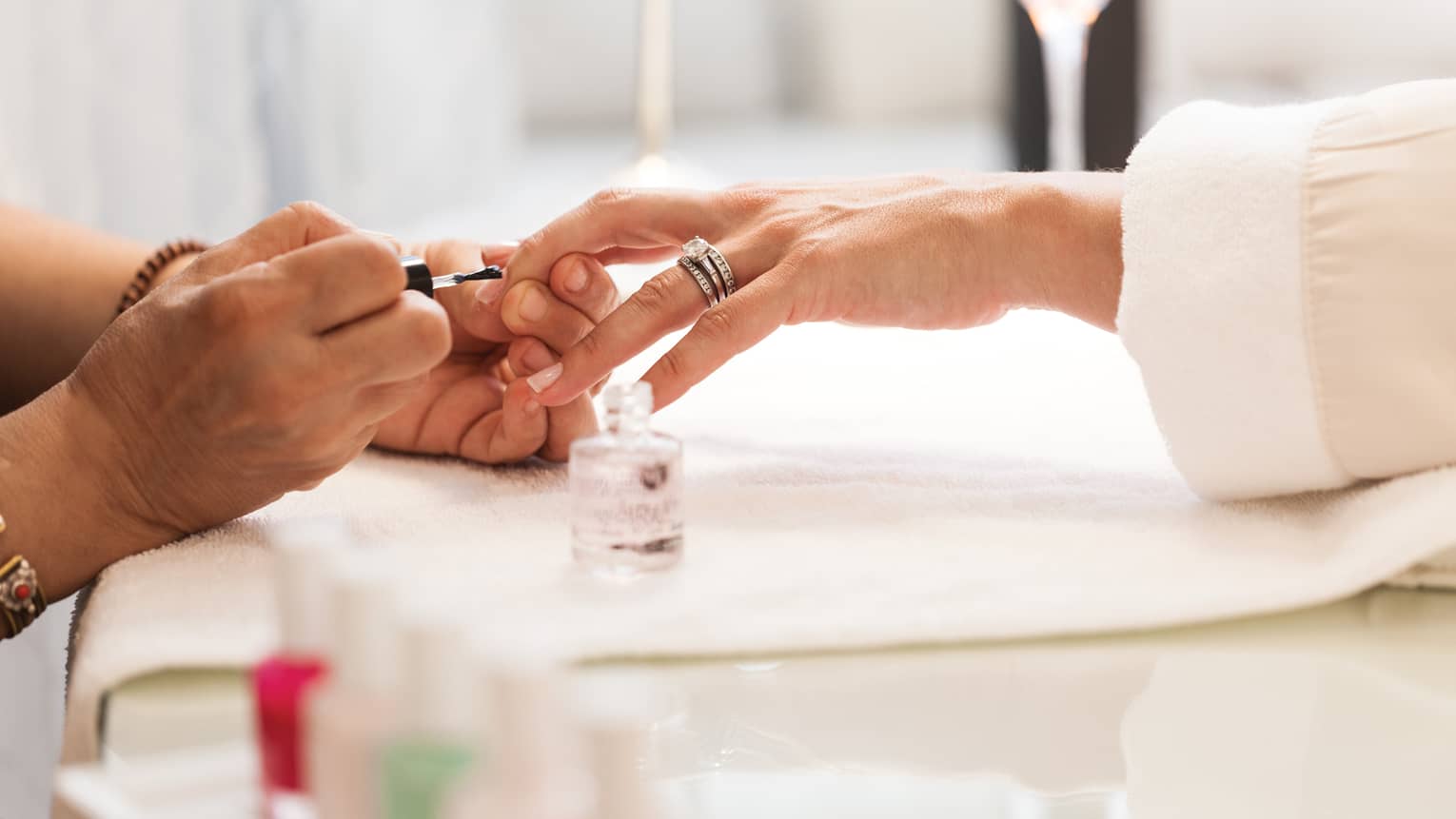 Close-up of woman in white robe getting clear polish manicure at spa table