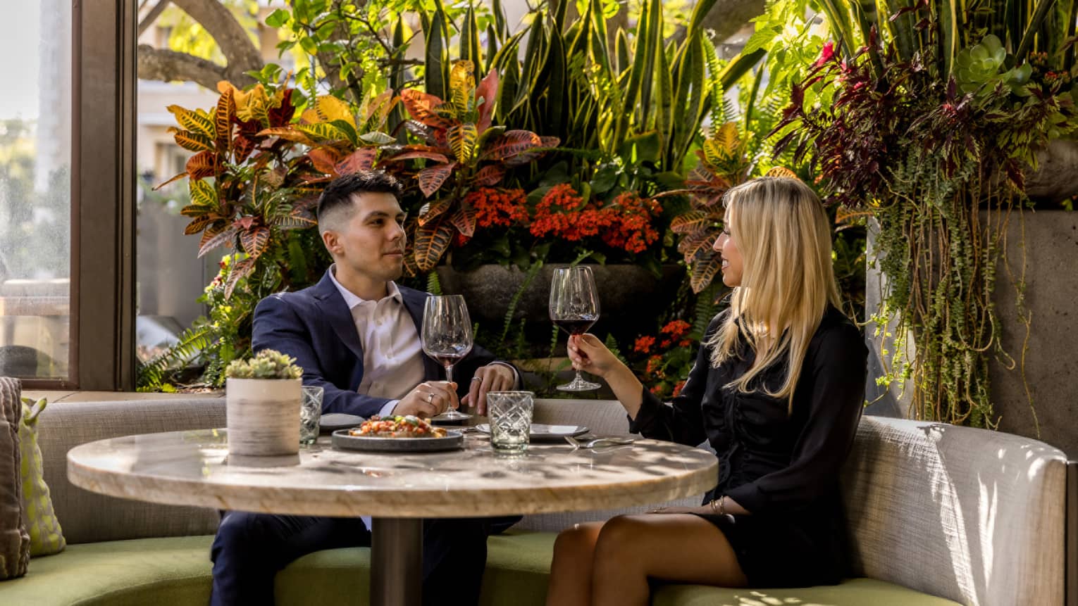 A man and woman sitting near flowers drinking wine.