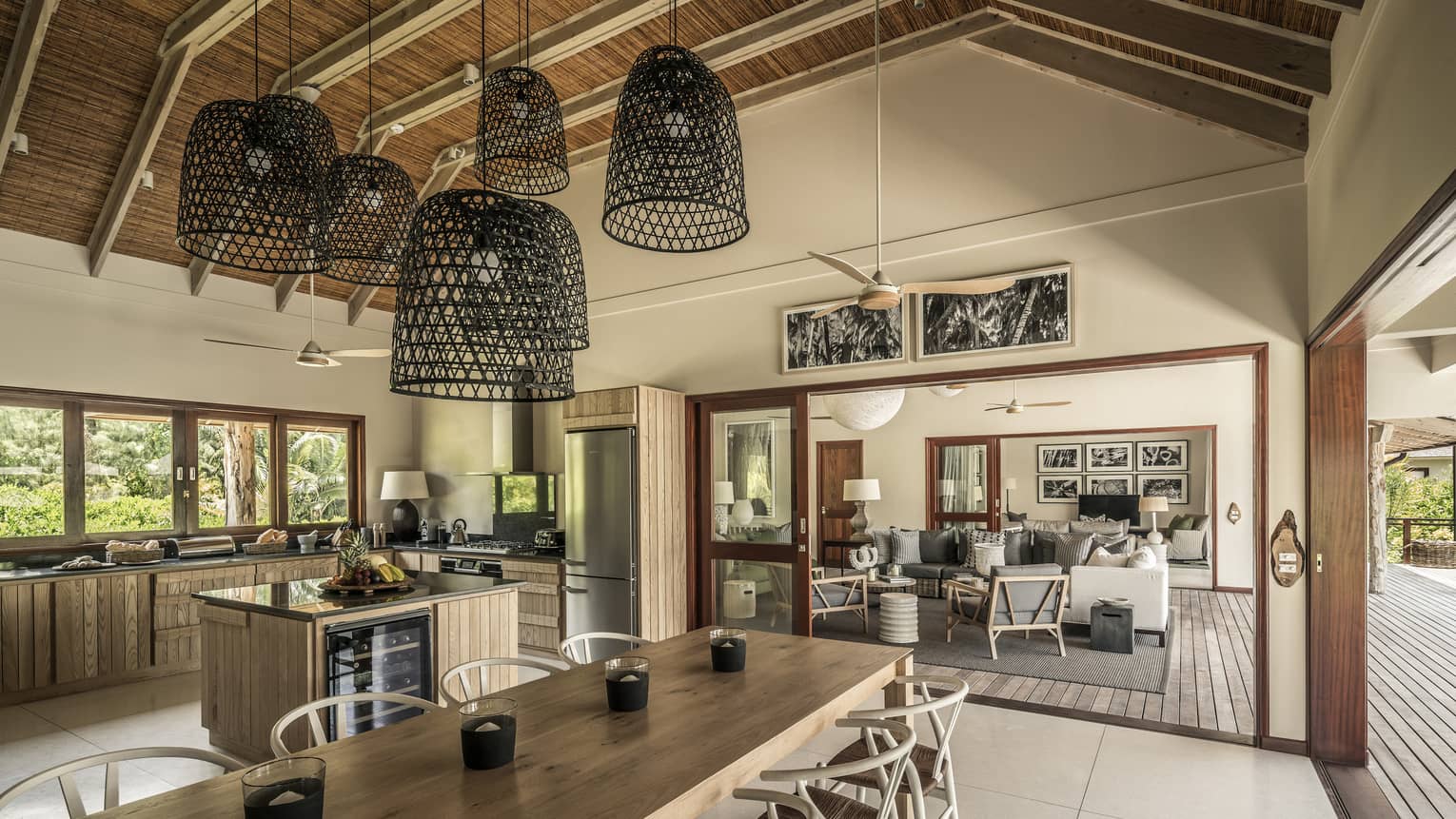 Large basket-like chandeliers hang from gambrel roof over long wood dining table, large kitchen
