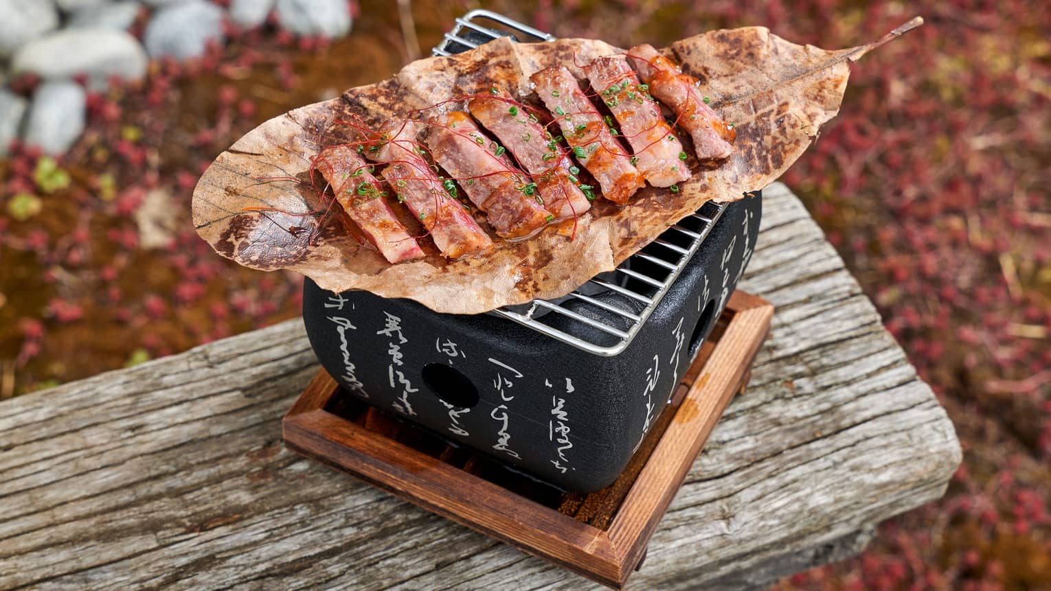 Sliced Wagyu beef on brown leaf atop square black grill