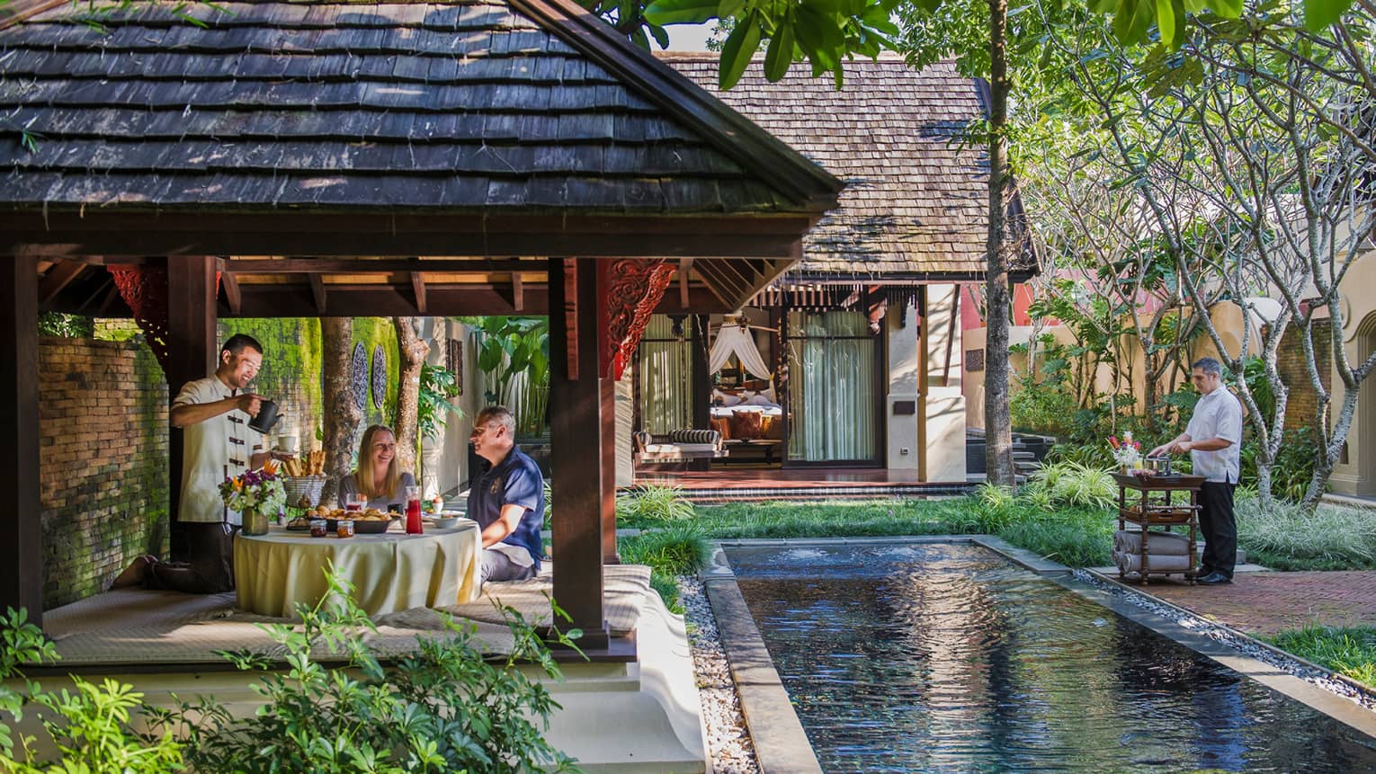 Hotel staff serve couple under dining gazebo by pond 