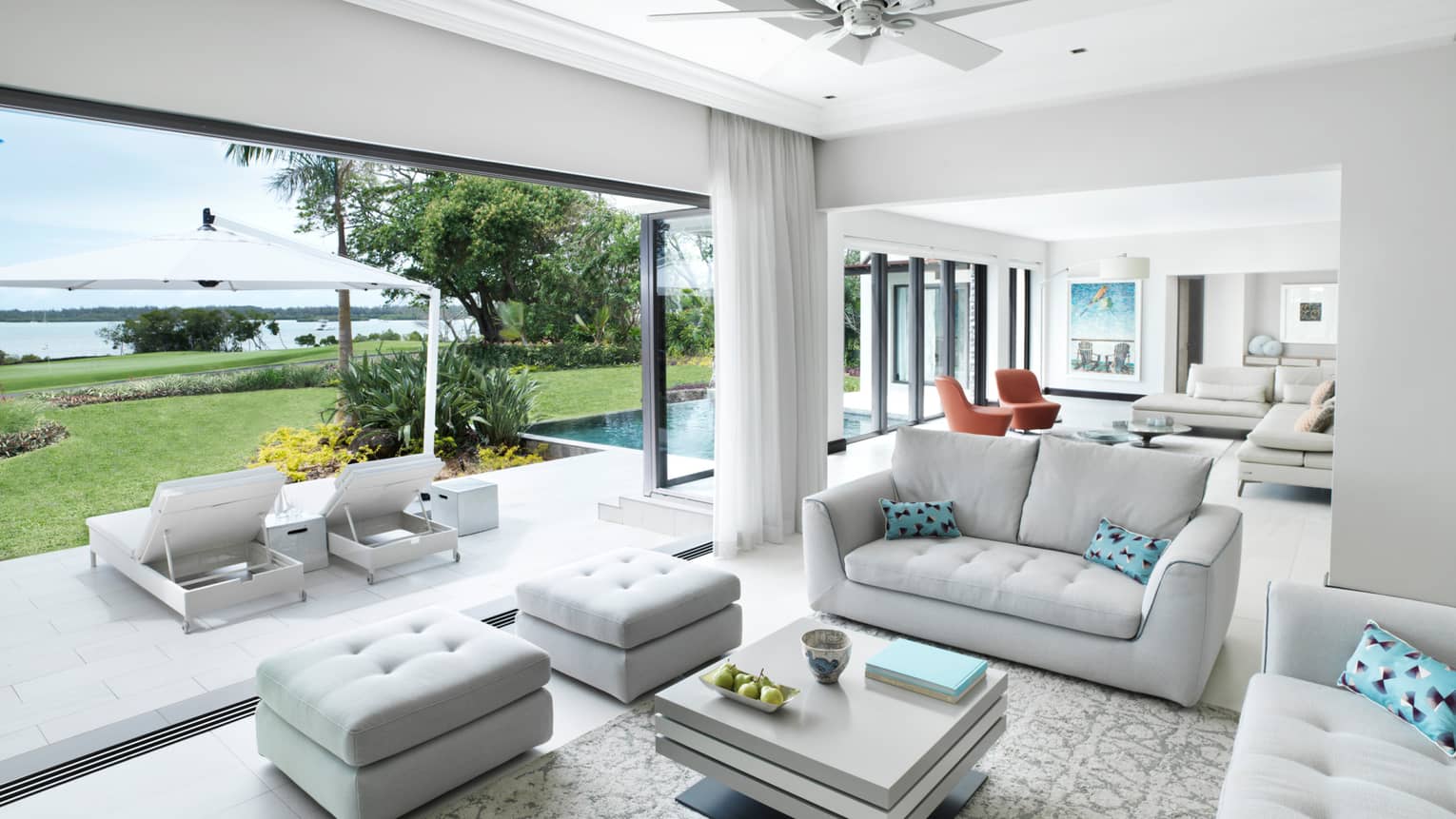 Suite with two white sofas, aqua pillows, two ottomans, square coffee table, patio and water view