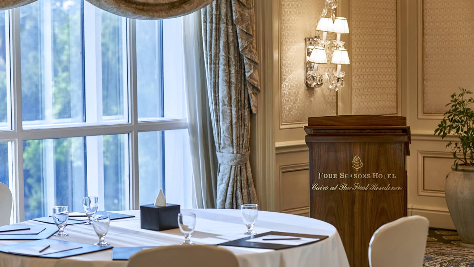 Round table by sunny window, speaker podium with Four Seasons Hotel Cairo at the First Residence logo